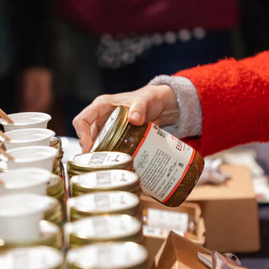 A person browses Big Spoon Roasters nut butters at a market. They are wearing red.