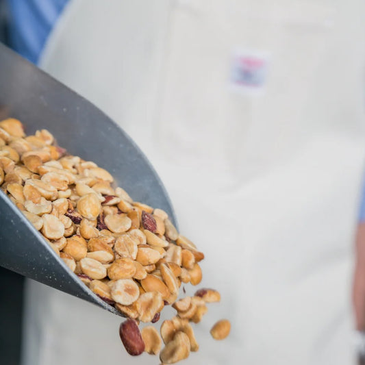 Peanuts pour out of a silver scoop in front of a white-aproned person