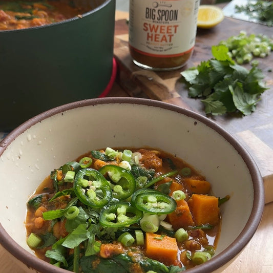 a bowl of vegan peanut stew sits surrounded by a jar of peanut butter, cilantro, and a dutch oven full of stew