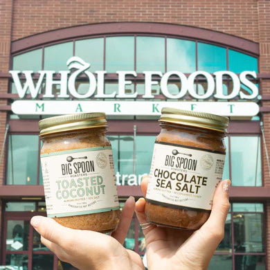 hands holding two Big Spoon jars in front of Whole Foods