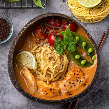 lum lum noodle dish in a bowl with noodles, lime, peas and tomatoes surrounding it