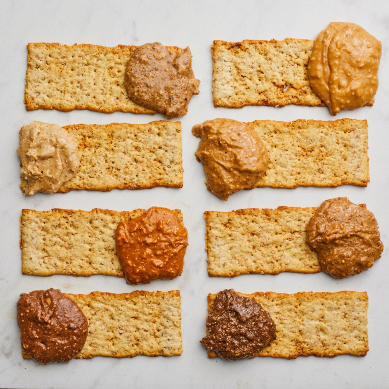 Nut Butters on a thin, rectangular crackers on a white marble surface