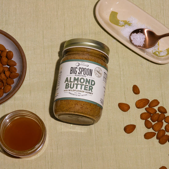 a jar of Almond Butter surrounded by a bowl of almonds, a jar of honey, sea salt, and other almonds
