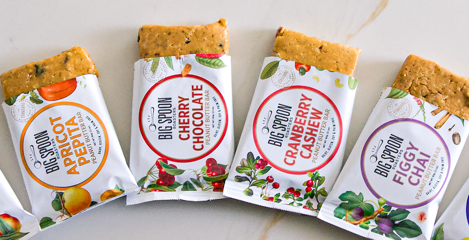 Four Big Spoon Roasters snack bars with colorful packaging on a marble surface.