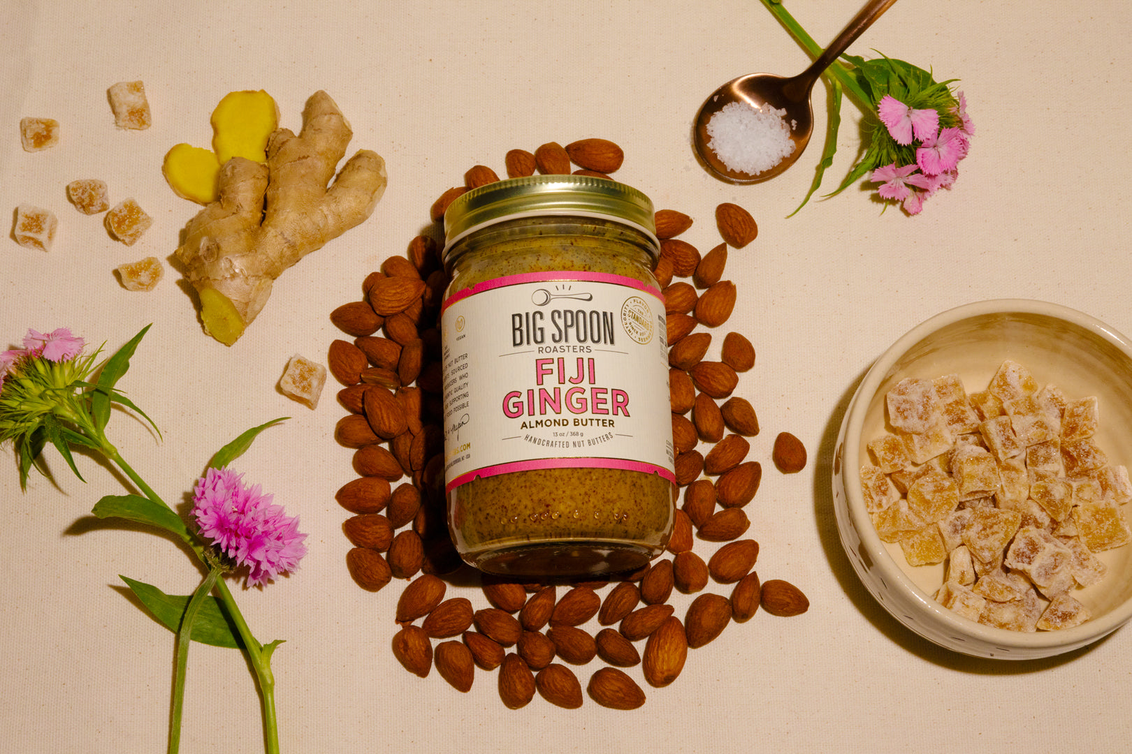 jar of Fiji Ginger Almond Butter surrounded by almonds, ginger, candied ginger, and sea salt
