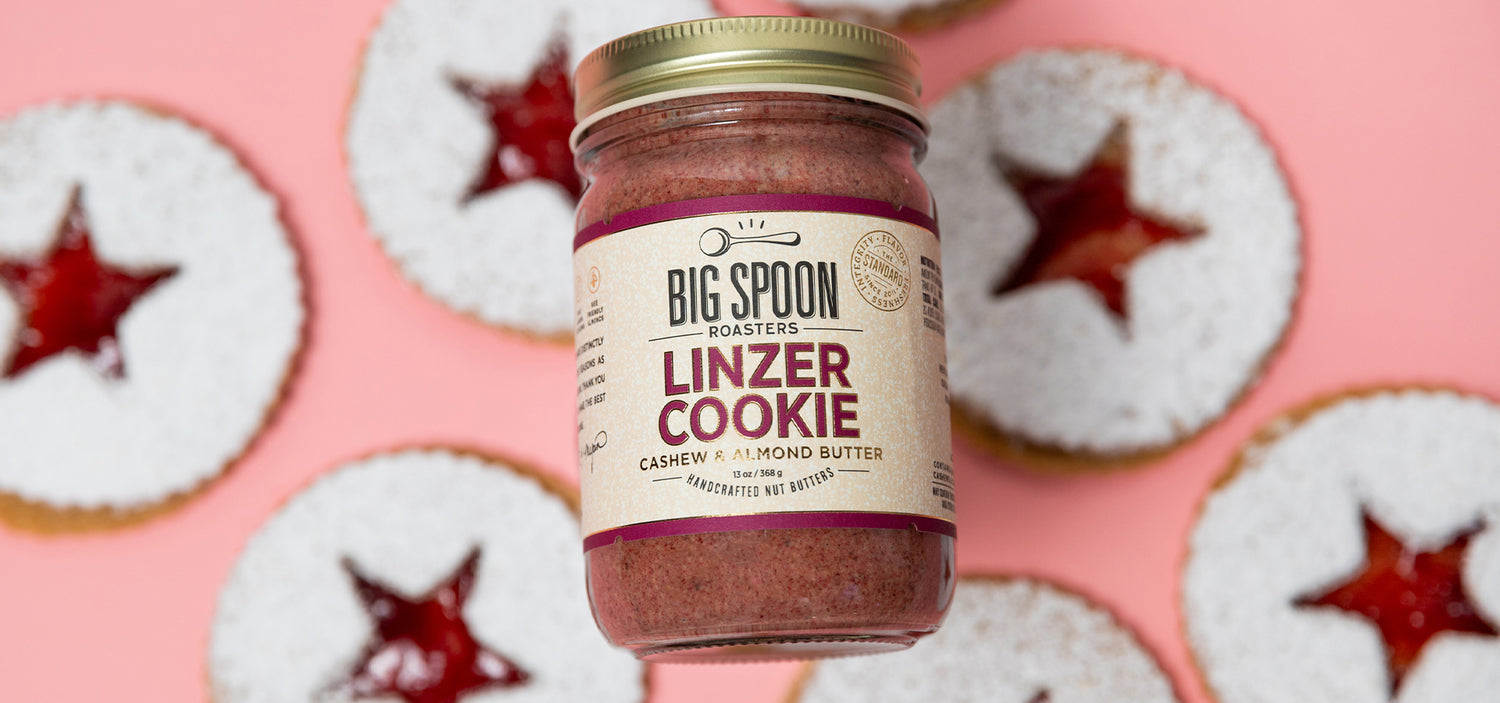 jar of Linzer Cookie Cashew & Almond Butter atop Linzer Cookies on a pink background