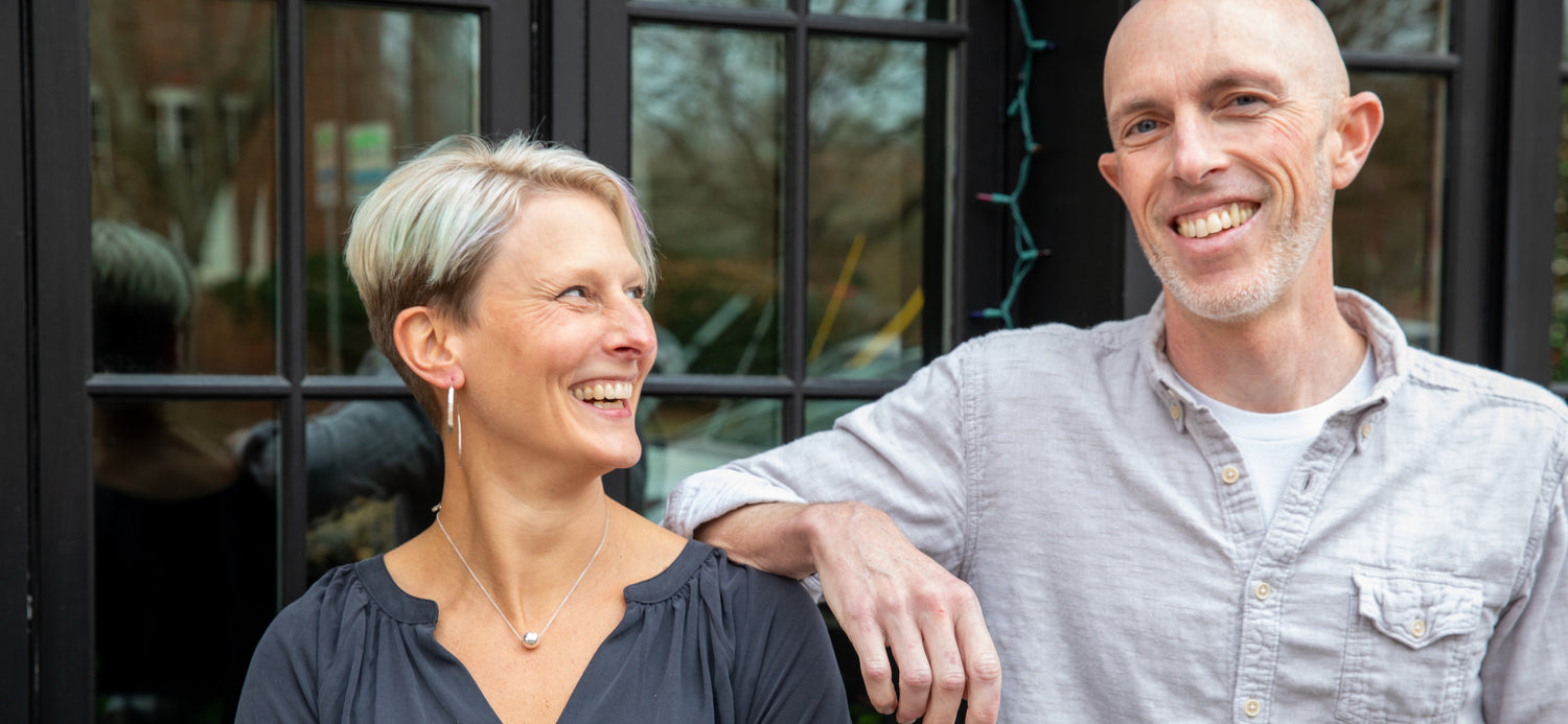 A woman smiles, looking over at a man who is smiling at the camera