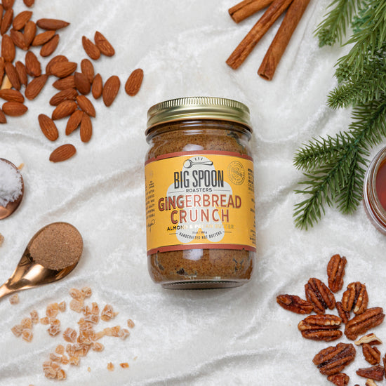 jar of gingerbread crunch almond & pecan butter with ingredients and pine branches scattered around