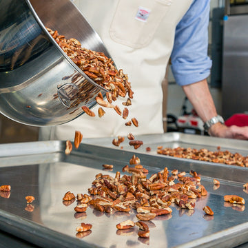 A man pours pecans out of a silver bowl onto a sheet pan