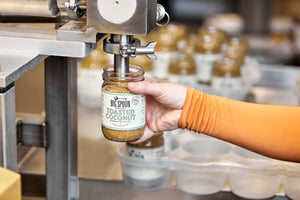 hand filling Toasted Coconut Almond Butter in production facility