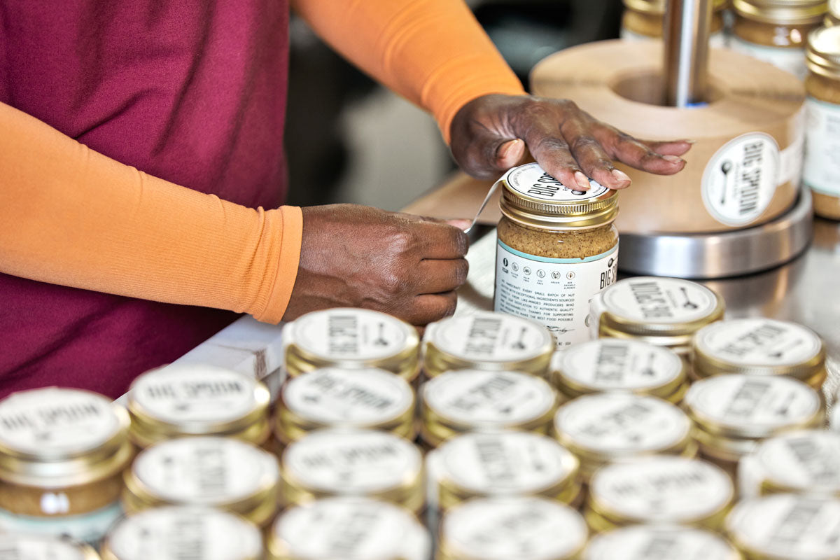 hands placing labels on jars of Toasted Coconut Almond Butter