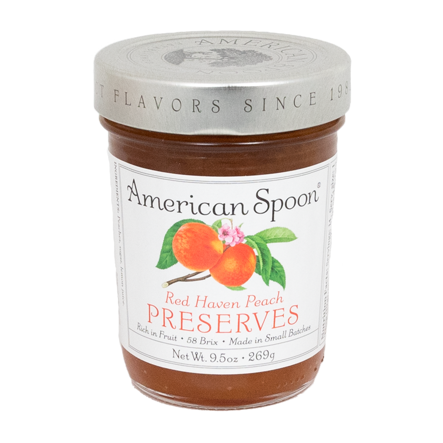 9.5 ounce jar of American Spoon Red Haven Peach Preserves in a glass jar with silver lid. Black font for logo and peach-y orange for the flavor name against a white label. Picture of two peaches on a branch with a peach flower depicted front and center on the label. 